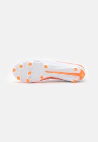 Talpa unei pantofi de sport albi cu cuie portocalii, având un design texturat și un logo Swoosh proeminent în portocaliu pe latură.