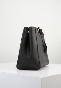 Svart läder axelväska med en strukturerad form, texturerad yta och detaljer i silver. Sidovy visar upp dubbla handtag.