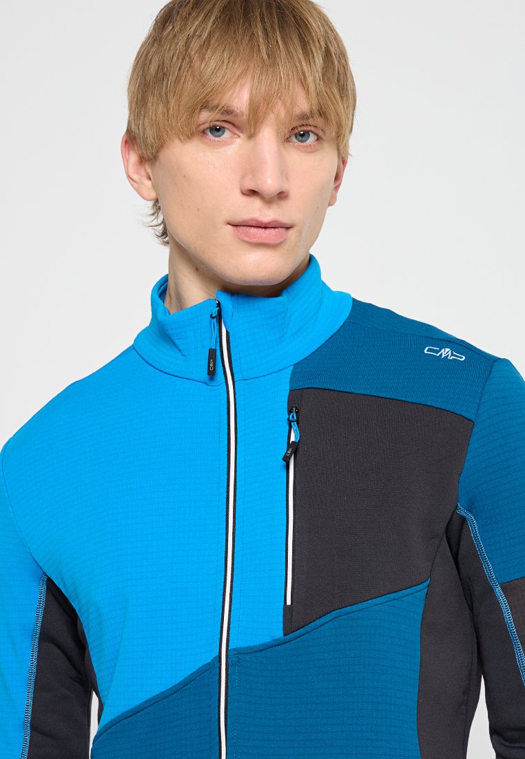 Chaqueta de forro polar azul y negra con un alto cuello, que presenta un cierre de cremallera y un bolsillo lateral. Tejido texturizado con paneles de color contrastante.