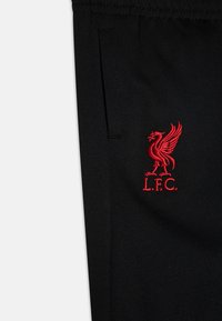 Pantalons de sport noirs en tissu doux avec un logo Liverpool FC brodé en rouge sur le bas à gauche. Comprend des poches latérales.