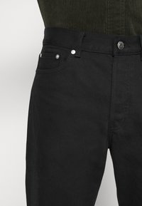 Černé džíny z denimu s klasickým designem, styl pěti kapes, s kovovými prvky stříbrné barvy a jemnou texturou.