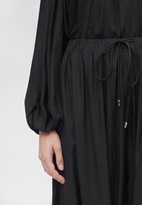 Gros plan de la main gauche d'une personne et d'une robe noire à manches longues avec une taille élastique et un cordon noué.