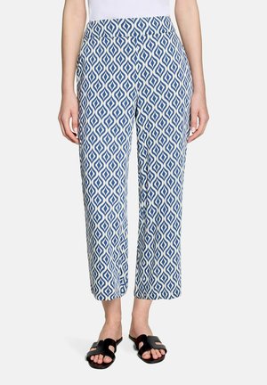 Slim-fit pants with blue and white geometric diamond pattern, worn with black slide sandals and white top.