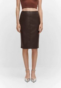 Jupe crayon en simili cuir marron avec une texture lisse, une coupe ajustée et une longueur au genou. Associée à des escarpins argentés à bout pointu.