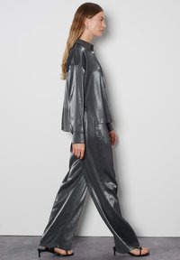 Completo grigio metallico composto da due pezzi, con una camicia a maniche lunghe con colletto e pantaloni a gamba larga, caratterizzato da una texture liscia e una leggera lucentezza.