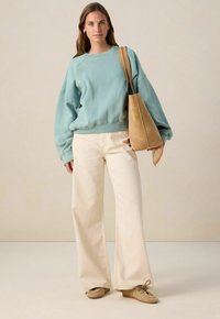 Sweatshirt oversize bleu clair avec un ourlet côtelé, associé à un jean large crème. Sac fourre-tout en suède beige avec une bandoulière et des chaussures lacées douces.