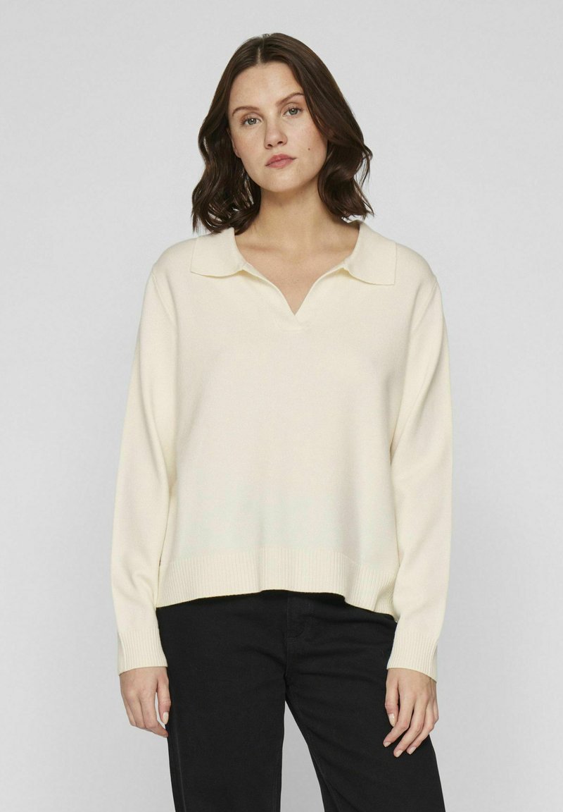 Ljusgrön pullover med v-ringning och platt krage, mjukt stickat tyg, sänkt axelsöm och ribbad fåll. Bärs med svarta byxor.