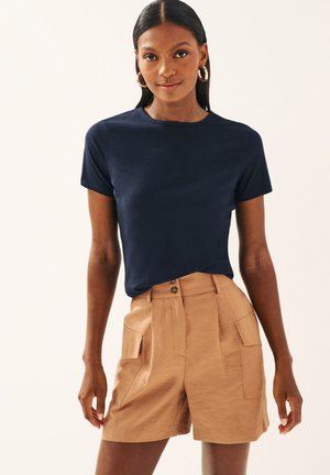 Marineblå kortärmad t-shirt kombinerad med bruna höga shorts med fickor och texturerad tyg.