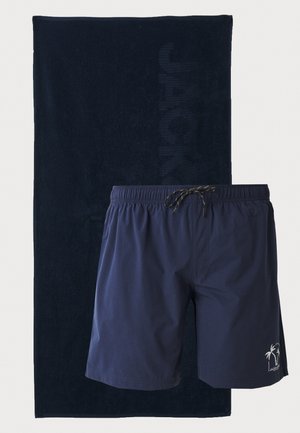 Tumesinine ujumispüksid elastse vöökoha ja paelaga, mille juurde kuulub sobiv tumesinine rätik, millel on peene logo kujundus.