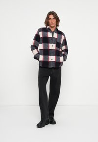 Fleece-Hemdjacke in Marineblau, Rot und Creme mit kariertem Muster, versehen mit Knöpfen und einem Kragen. Kombiniert mit schwarzen weit geschnittenen Jeans und schwarzen Schuhen.