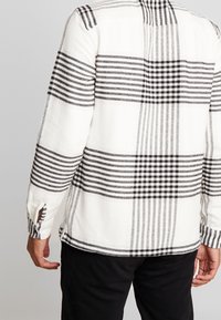 Witte en zwarte geruite flanellen shirt met een zachte textuur, voorzien van lange mouwen en knoopdetails op de manchetten.