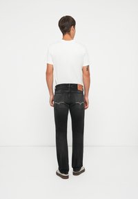 Black denim jeans with a straight leg fit, featuring light stitching and a leather patch on the back. Worn with a plain white T-shirt.