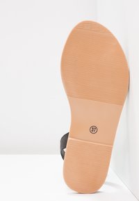 Semelle d'une chaussure beige avec une semelle texturée, taille 37 indiquée au centre, bride noire partiellement visible sur fond blanc.
