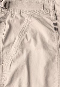 Lichtbeige shorts van zacht materiaal met zichtbare stiksels, schuin geplaatste zijzakken en twee decoratieve metalen knopen nabij de tailleband.