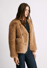 Braune Kunstfelljacke mit einem doppelt knöpfbaren Design, rundem Kragen, zwei Fronttaschen und weichem, strukturiertem Stoff.