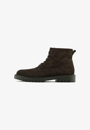 Bottines en suède marron foncé avec un bout rond, un laçage à l'avant et une semelle en caoutchouc dotée de reliefs prononcés pour une meilleure adhérence.