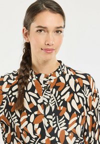 Button-up shirt featuring a multi-colored abstract leaf pattern in orange, cream, and black on a lightweight fabric; band collar detail.