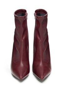 Pár bordó kožených kotníkových bot s špičatými špičkami a bočními zipy, zobrazené zepředu na bílém pozadí.