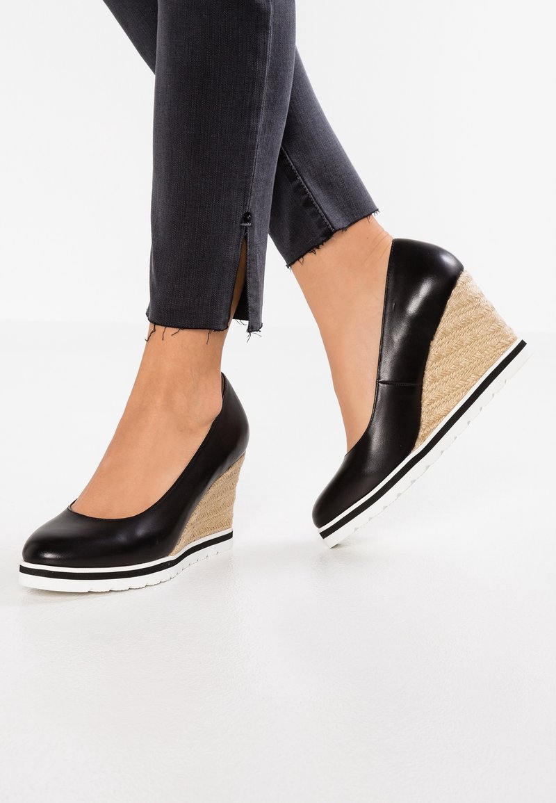 Chaussures compensées en cuir noir avec une semelle en liège texturée, une bande blanche en accent, un bout arrondi, portées avec un jean foncé légèrement effiloché.