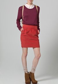 Jersey burdeos con cuello redondo y camisa de crema debajo; falda de sarga roja con pliegues; botas de tacón marrones hasta el tobillo.