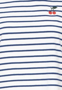 Bílá látka s pravidelně rozestoupenými horizontálními tmavomodrými pruhy a malou vyšívanou červenou třešní se zelenými listy poblíž pravého horního rohu.