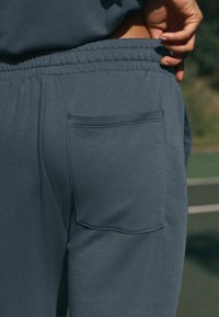 Donkergrijze sweatpants met een zijzak, elastische tailleband en een zachte stoftextuur, met een schone, minimalistische uitstraling.