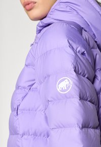 Giacca a vento viola con texture trapuntata. Presenta un cappuccio e un logo bianco di un elefante sulla manica sinistra. Materiale resistente.