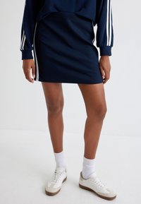 Gonna navy con strisce laterali bianche, realizzata in un tessuto morbido. Abbinata a sneakers bianche e calzini bianchi a coste, mette in risalto un look casual.