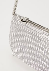 Borsa argentata con superficie texturizzata composta da piccoli strass, dotata di tracolla in catena metallica e dettaglio ad occhio nella parte superiore.