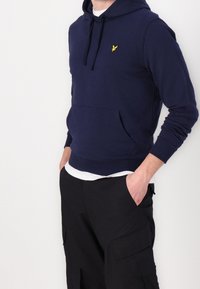 Sudadera con capucha de forro polar azul marino, con un bolsillo frontal, capucha con cordón y un pequeño logo amarillo en el pecho. Mangas largas y ajuste relajado.