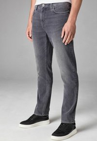 Harmaat denim-farkut, joissa on slim fit -leikkaus, viisi taskua ja hienovaraista haalistumista. Yhdistetty mustiin lenkkareihin, joissa on kontrastina valkoinen pohja.