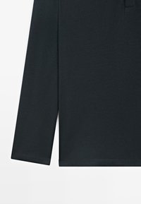 Manica lunga nera e orlo di una camicia in cotone semplice su sfondo bianco.