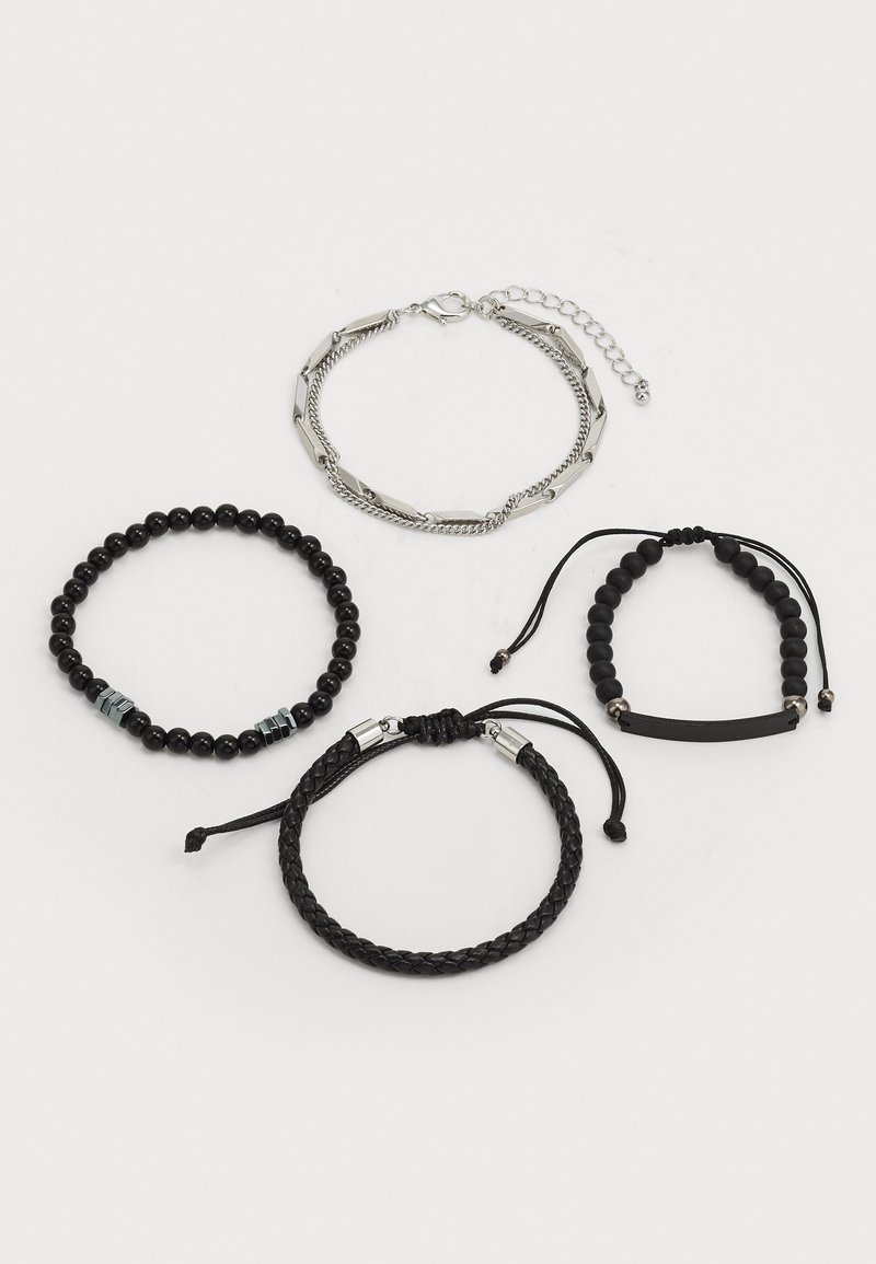 Cuatro pulseras: una cadena de plata, una pulsera de cuentas negras con acentos metálicos, un estilo trenzado de cuero negro, y una banda delgada negra con cuentas.