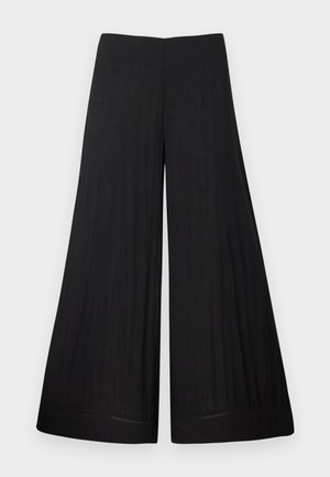 Pantalon noir à larges jambes en tissu léger. Il possède une taille plate et un matériau fluide, avec peu de détails de couture.
