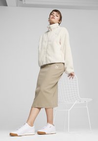 Giacca in pile bianca con colletto alto, gonna beige a coste e sneakers bianche con suola in gomma. Design semplice e pulito, con colori neutri.