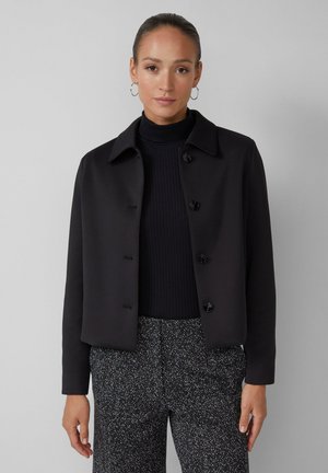 Black cropped jacket with a collared neckline, front button closure, and textured fabric, worn over a ribbed turtleneck.