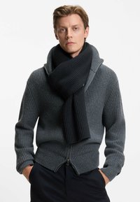 Grå strikket cardigan med sjalskrave, med lynlåslukning og ribbet tekstur. Parret med en ensfarvet sort ribbet tørklæde.