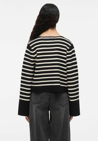Maglione a righe nero e crema con un design accorciato e maniche a sbuffo, realizzato in un morbido materiale lavorato a maglia. Vista posteriore, che mostra un ampio scollo.