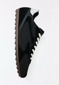 Baskets noires avec lacets blancs, semelle texturée marron et détail blanc au talon, vues de côté sur fond blanc.