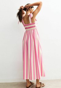 Maxikleid mit pink-weißem Streifenmuster, gesmoktem Rücken und schleifenartigen Trägern. Aus weichem Baumwollmaterial, fließendem Design und knöchellang.