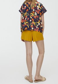 Short-sleeve, navy top with fruit pattern; paired with mustard yellow shorts. Flat sandals with woven detail. Simple and relaxed fit.