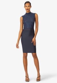 Marineblaues Kleid mit einer figurbetonten Silhouette, hohem Hals und Nieten-Design im oberen Bereich. Geschmeidiger, dehnbarer Stoff mit einem knielangen Bleistiftrock.