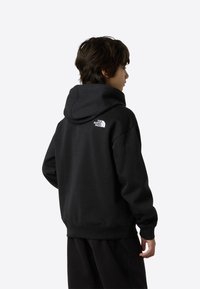 Hanorac negru din material moale, cu glugă mare, manșete ribbed și un logo alb pe partea superioară a spatelui. Asortat cu pantaloni negri.