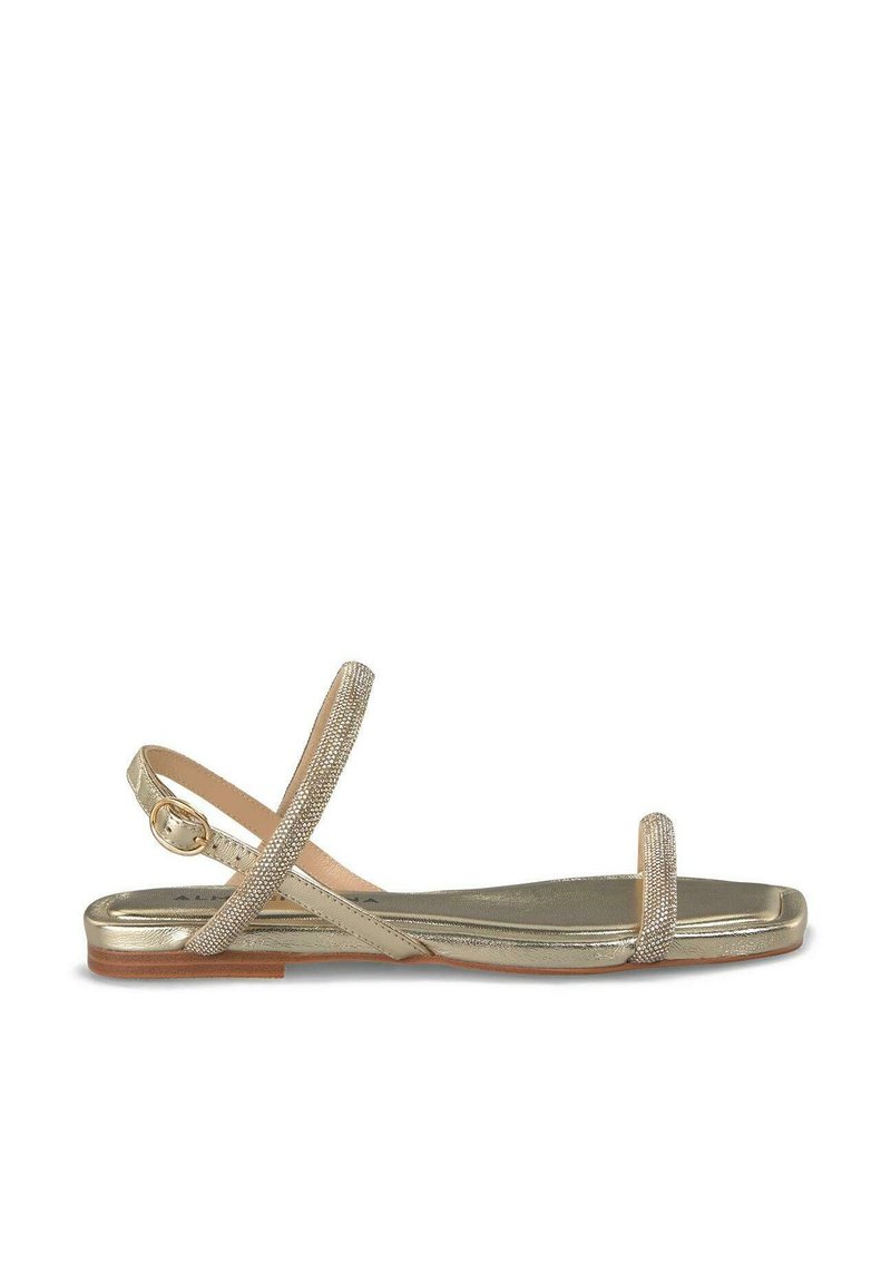 Metaliczne złote płaskie sandały z delikatnym wzorem krzyżowych pasków. Teksturowane paski z subtelnym połyskiem, z zapięciem na klamrę.