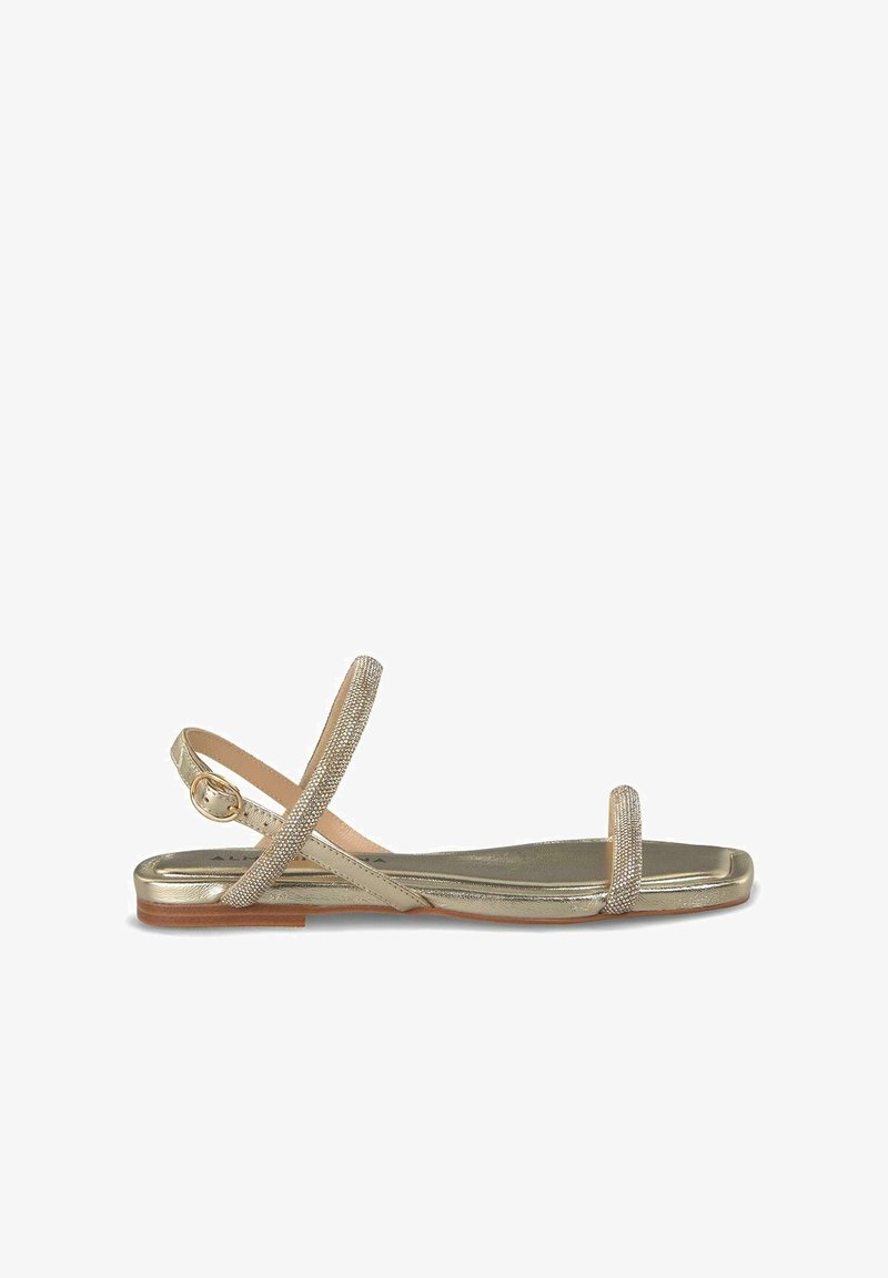 Metallisch goldene flache Sandalen mit einem zarten Kreuzriemendesign. Texturierte Riemen mit einem subtilen Schimmer, ausgestattet mit einem Schnallenverschluss.