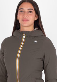 Bruine ritssluiting jas met een capuchon, voorzien van een meerkleurige rits en een logo op de borst. Soepele, lichte stof met een aangesloten ontwerp.