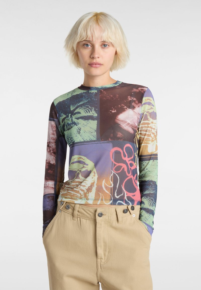 Long-sleeve top featuring a multicolored graphic print with abstract designs, made of stretch fabric, paired with beige trousers.