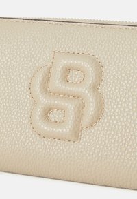Beigās ādas maks ar teksturētu virsmu un izteiktu uzspiedu logotipu. Apdarināts ar kontrastējošiem šuvēm gar malām.