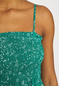 Robe verte à imprimé floral blanc, avec une texture froncée et des bretelles fines, réalisée en tissu léger.