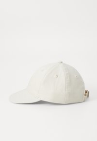 Beige bomullsbasketcap med en böjd skärm, sex tygpaneler och ett justerbart band bak. Har ventilationshål på toppen.